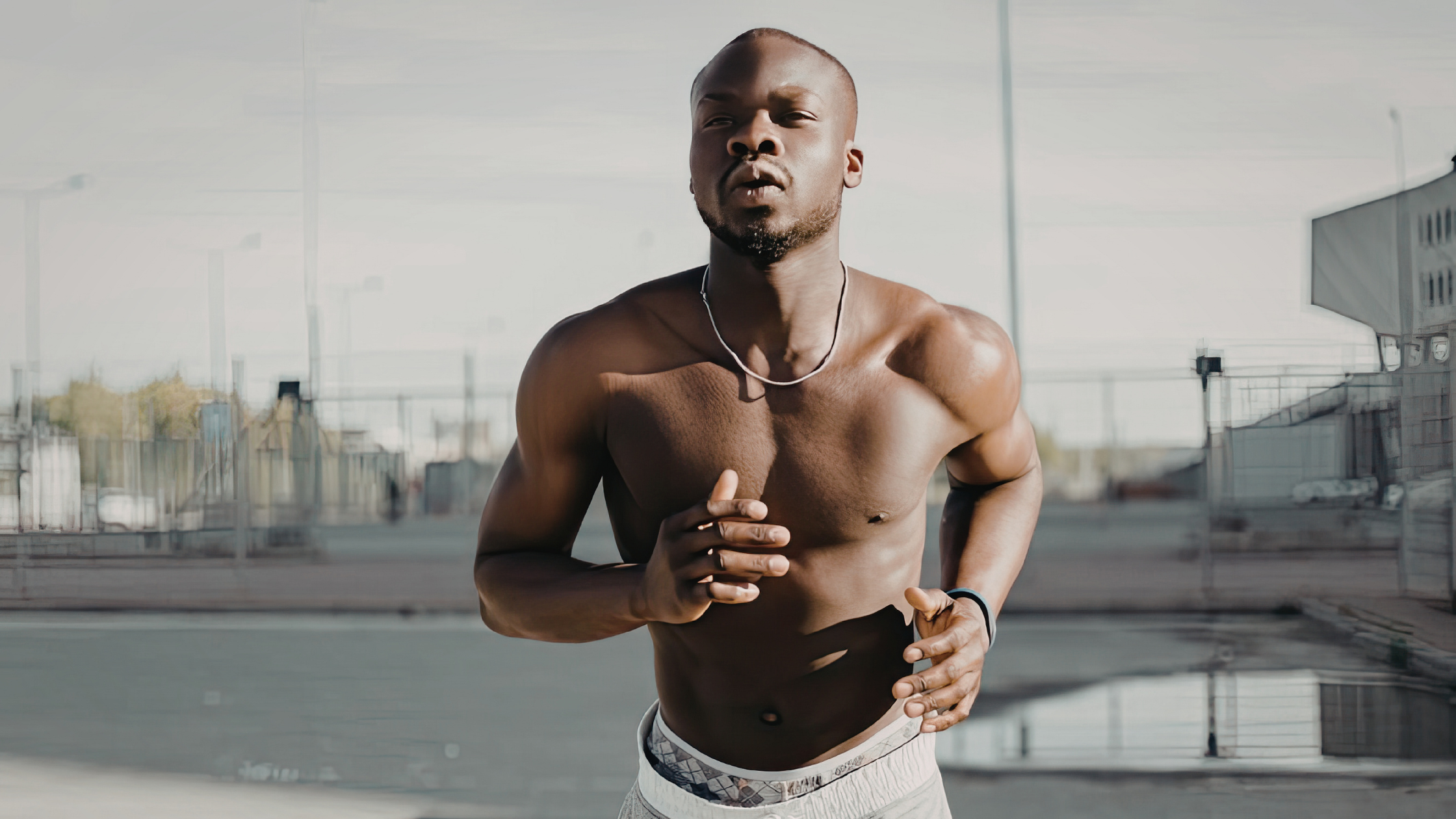 Athlete running shirtless on a track with urban background